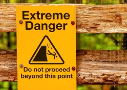 Yellow warning sign reading 'Extreme Danger. Do not proceed beyond this point' mounted on a weathered wooden barrier.