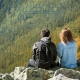 WhySIEM - Go West IT Two people with backpacks sit on rocky ground, facing a glowing circuit-board pattern representing technology and exploration.