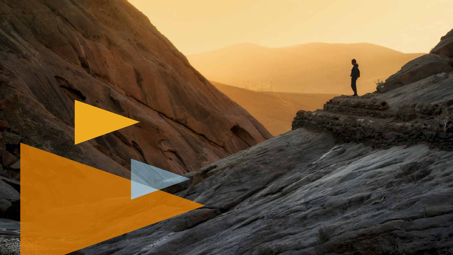 AI App Hosting for Businesses: Where Should Your AI-Built Applications Live? - Go West IT Hiker stands on a rocky ridge at sunset, with orange geometric shapes in the foreground.