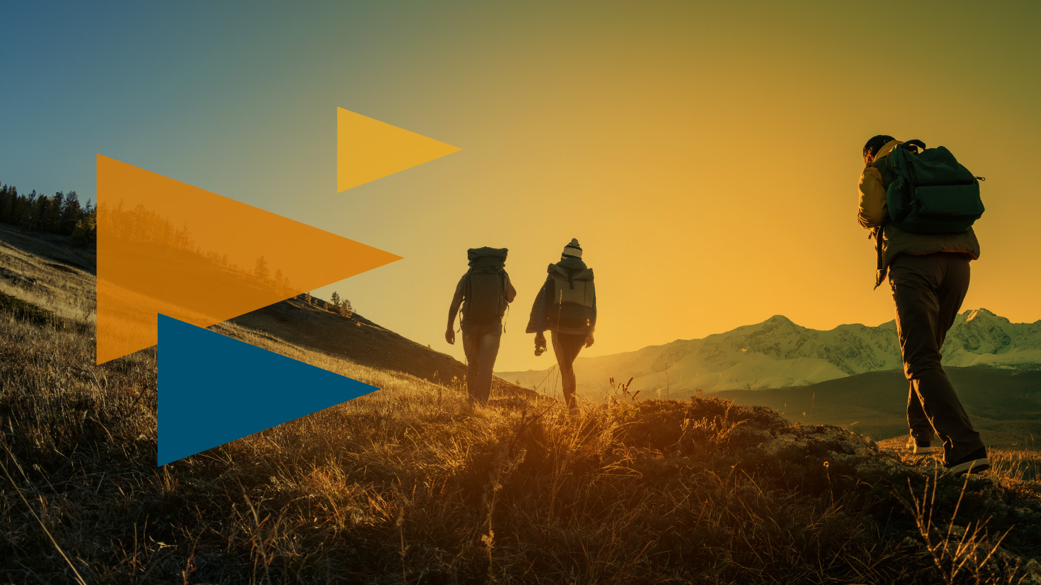 Three hikers with backpacks walk across a sunlit hillside at sunset toward distant mountains with a warm gradient sky.