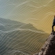 Hiker stands on a rocky peak overlooking a valley with abstract contour lines across the scene.